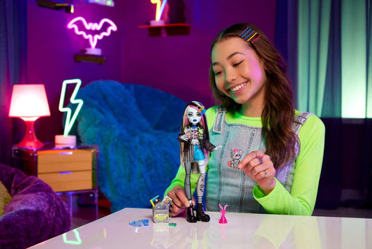 Monster High Frankie Stein doll in denim jacket and shorts, includes her dog Watzie and accessories like a backpack, snack, and notebook. HXH73.